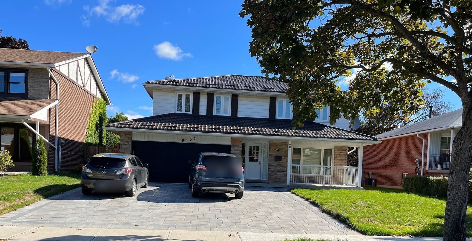 Two-storey home with a new dark shingle roof, white eavestrough and stone porch