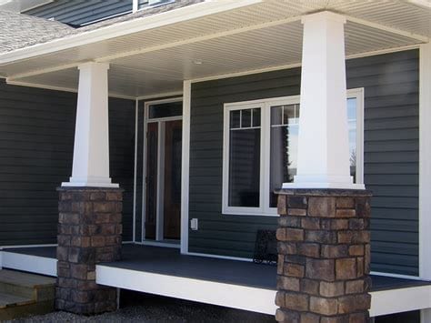 Decorative white porch columns with stone bases on a dark-sided home